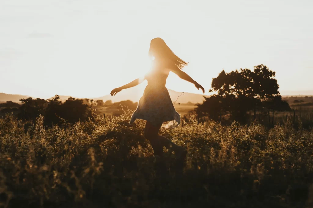 Woman twirling in a field at sunrise or sunset.